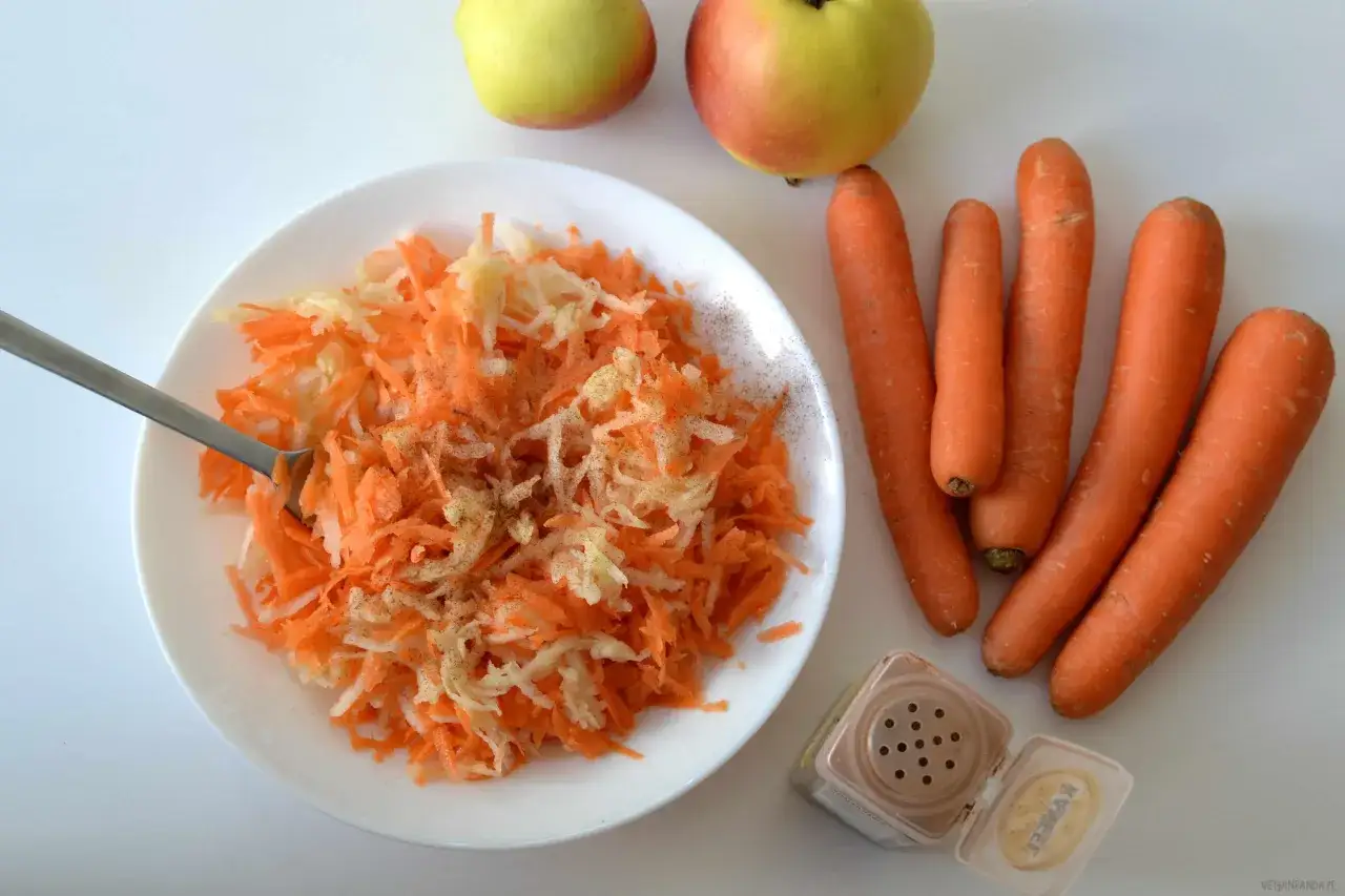 Surówka z marchewki jak z restauracji, z jabłkiem i przyprawami. Obok leżą świeże marchewki i jabłka.