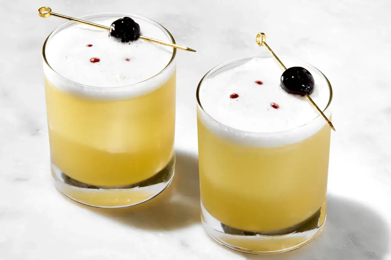 Dwa orzeźwiające koktajle: Whisky Sour i Amaretto Sour, z pianką i wiśnią na patyczku.