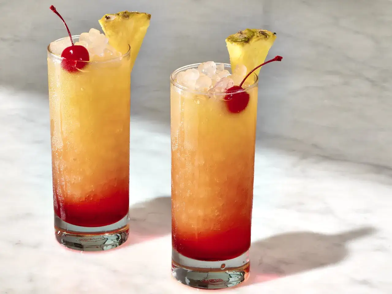Dwa orzeźwiające drinki z malibu, z lodem, wiśnią i kawałkiem ananasa, idealne na letnie popołudnie.