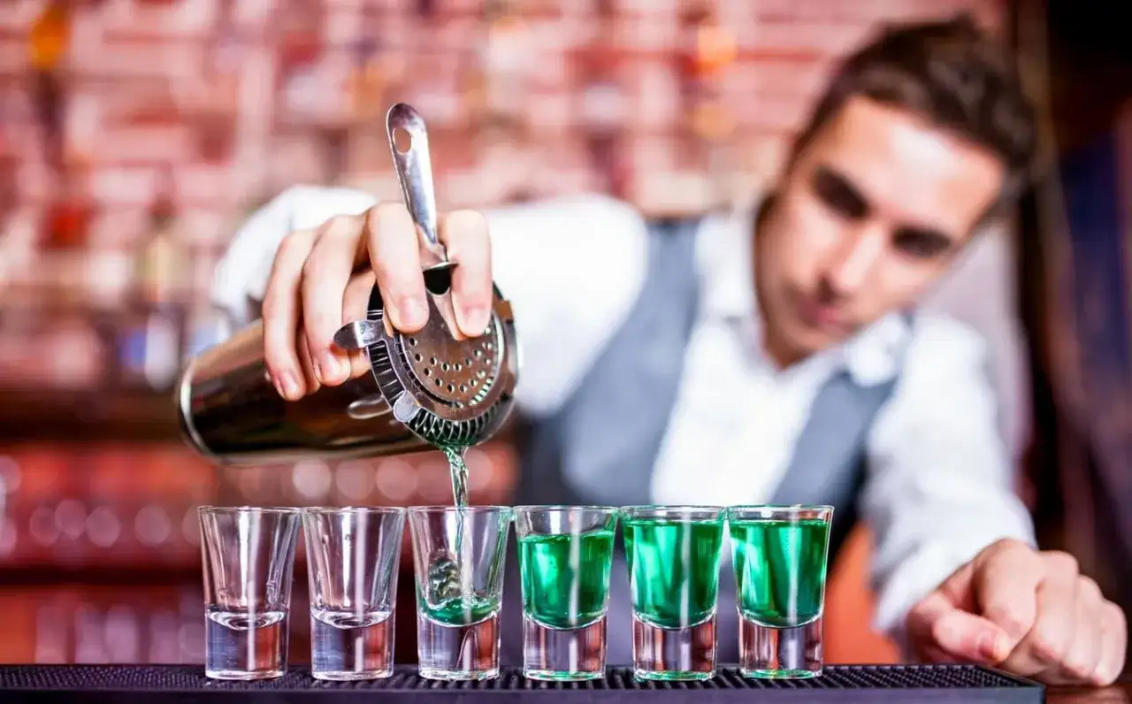 Barman nalewa zielony shot. Czy barman może pić w pracy? To pytanie, na które odpowiedź zależy od zasad lokalu i jego odpowiedzialności.