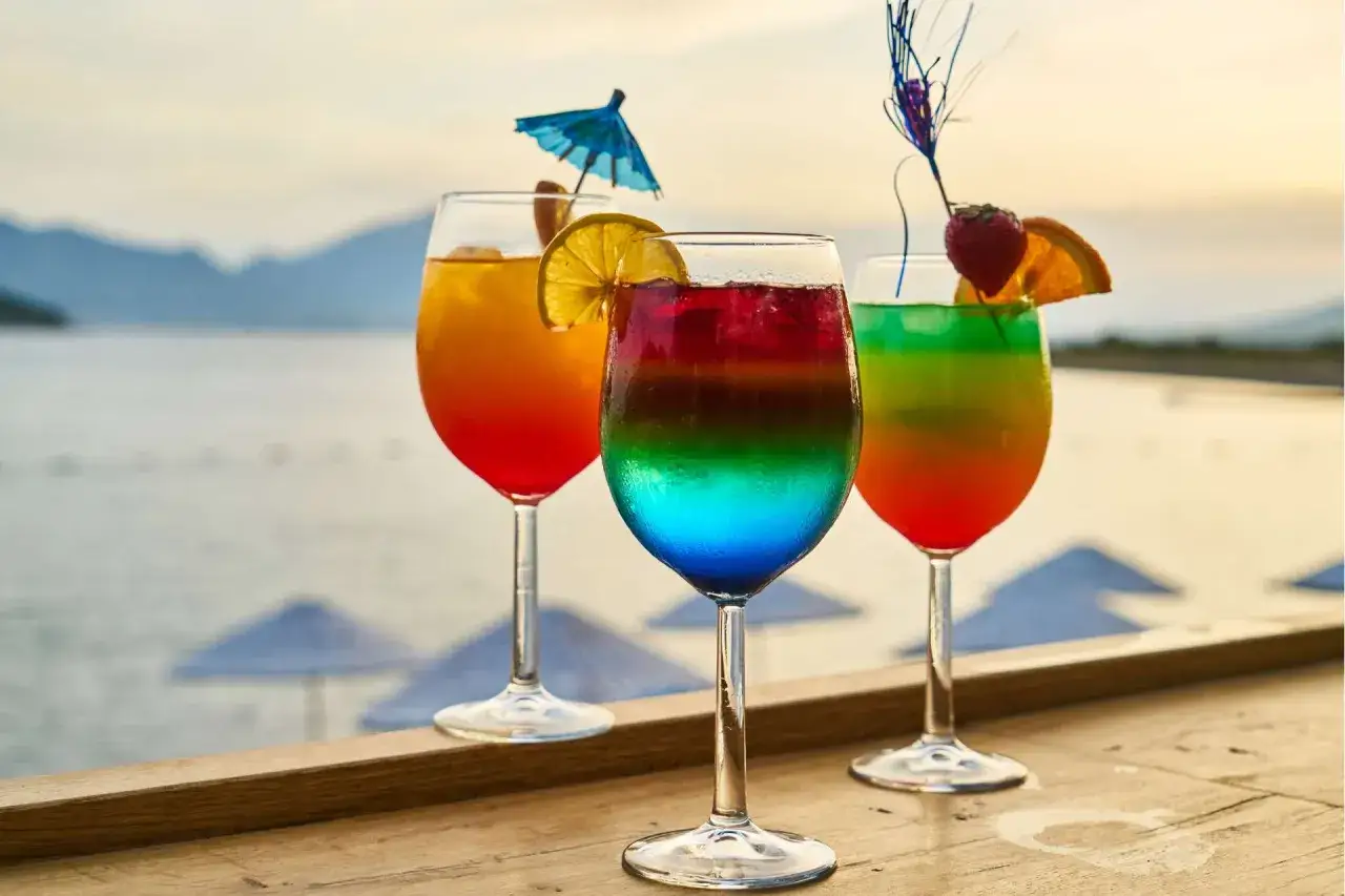 Kolorowe drinki z parasolką i owocami na tle morza i gór. Idealne na wakacyjny relaks.