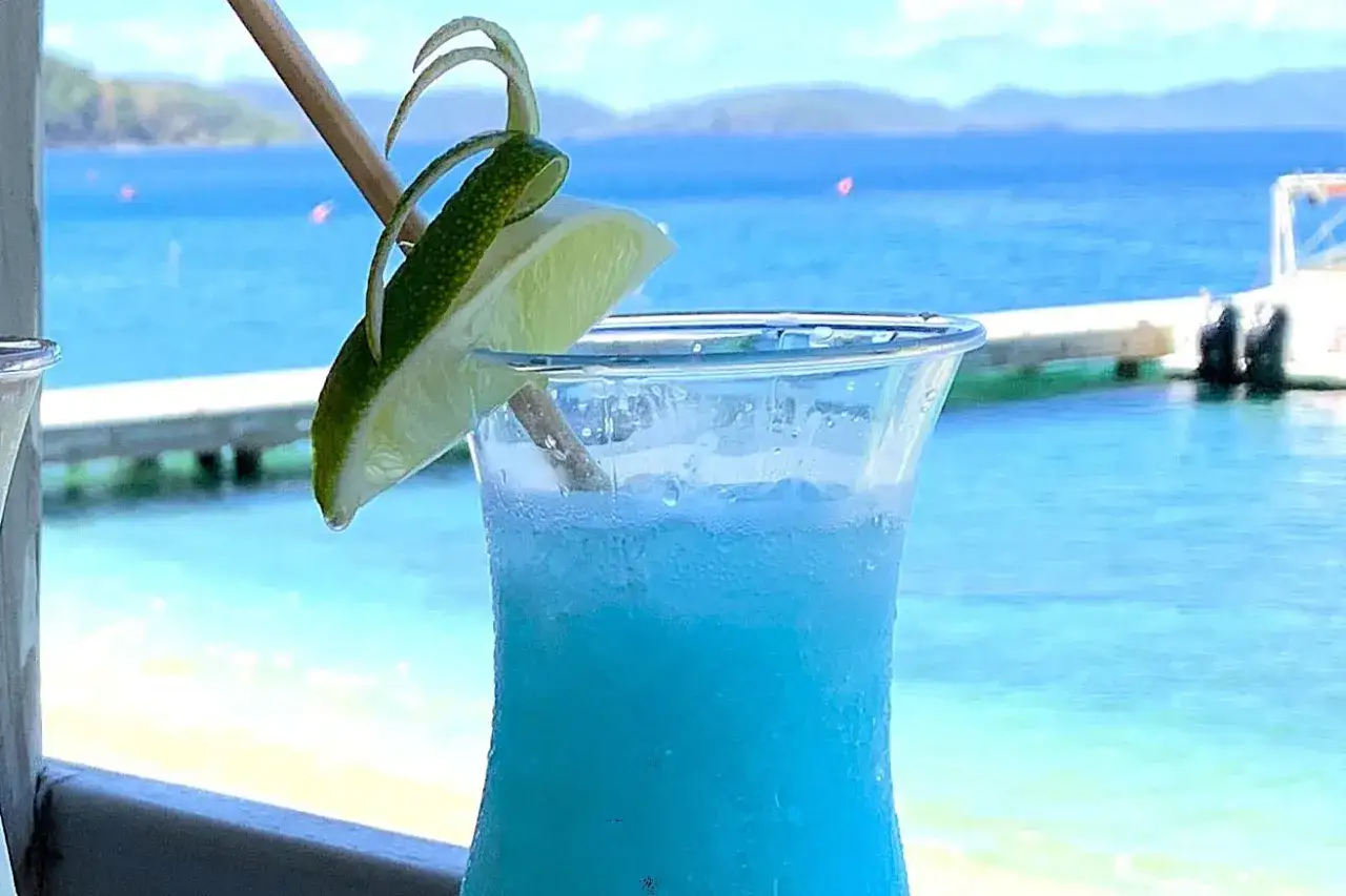 Niebieski drink z malibu z mlekiem, ozdobiony limonką, na tle błękitnego morza i plaży. Idealny na wakacje.
