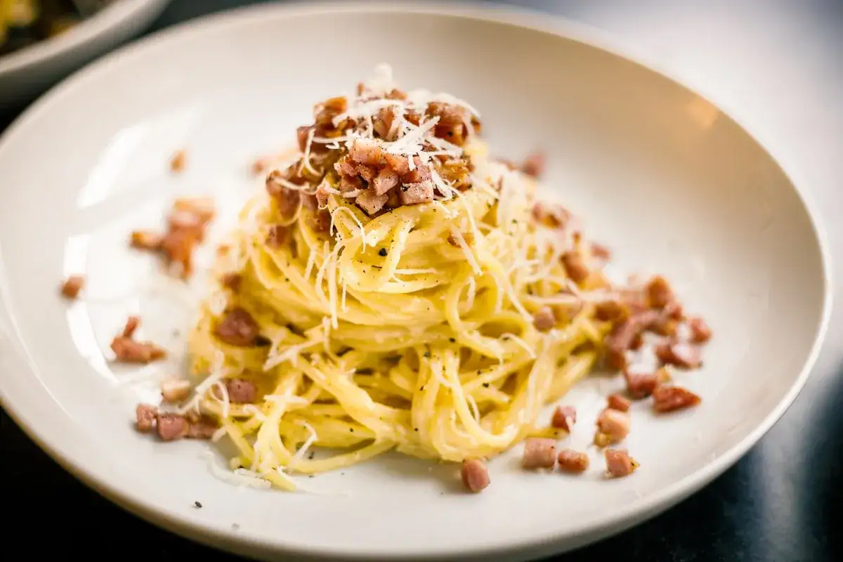 Pyszne Spaghetti Carbonara przepis. Makaron z boczkiem, parmezanem i pieprzem na białym talerzu.
