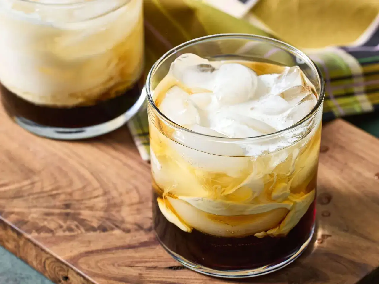 Dwa szklanki z lodem i kremowym, warstwowym drinkiem. Jeden z nich to biały rusek drink, idealny na wieczór.