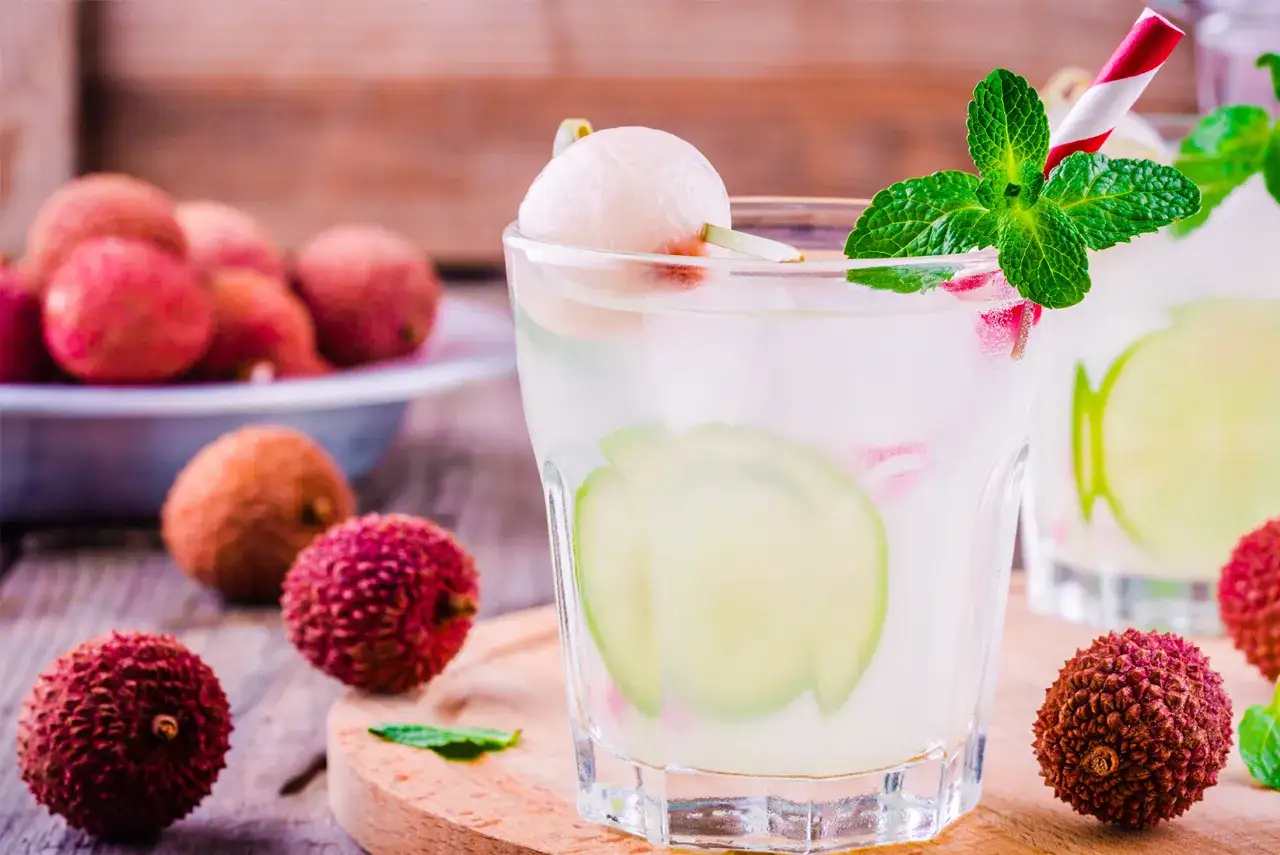Orzeźwiające drinki z liczi, ozdobione miętą i plasterkami limonki. Na stole świeże owoce liczi.