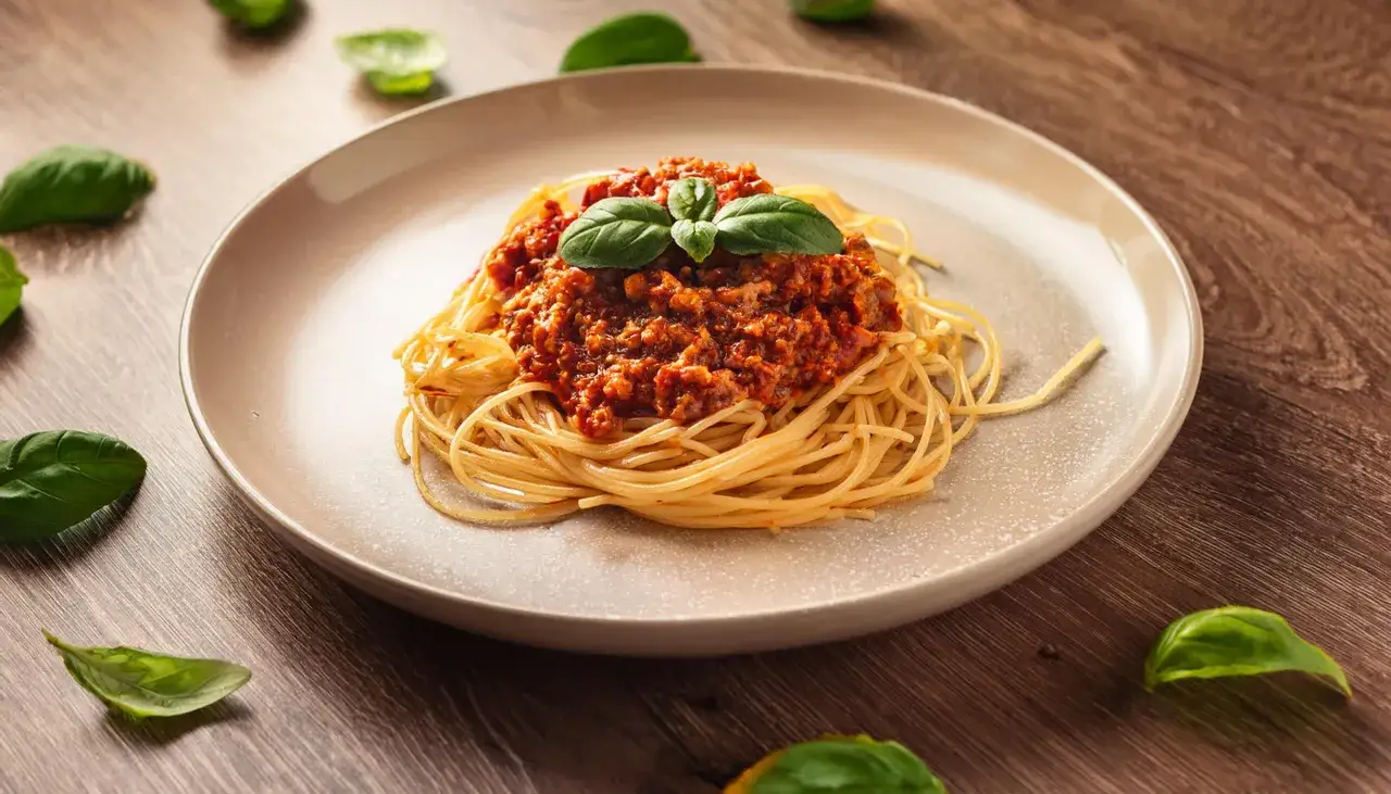 Pyszne spaghetti z sosem bolońskim, przygotowane z przyprawą do spaghetti Knorr, ozdobione listkami bazylii.