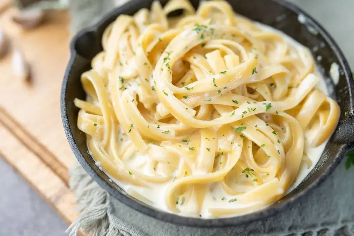 Pyszne spaghetti bez mięsa w kremowym sosie, posypane natką pietruszki, podane w żeliwnej patelni.
