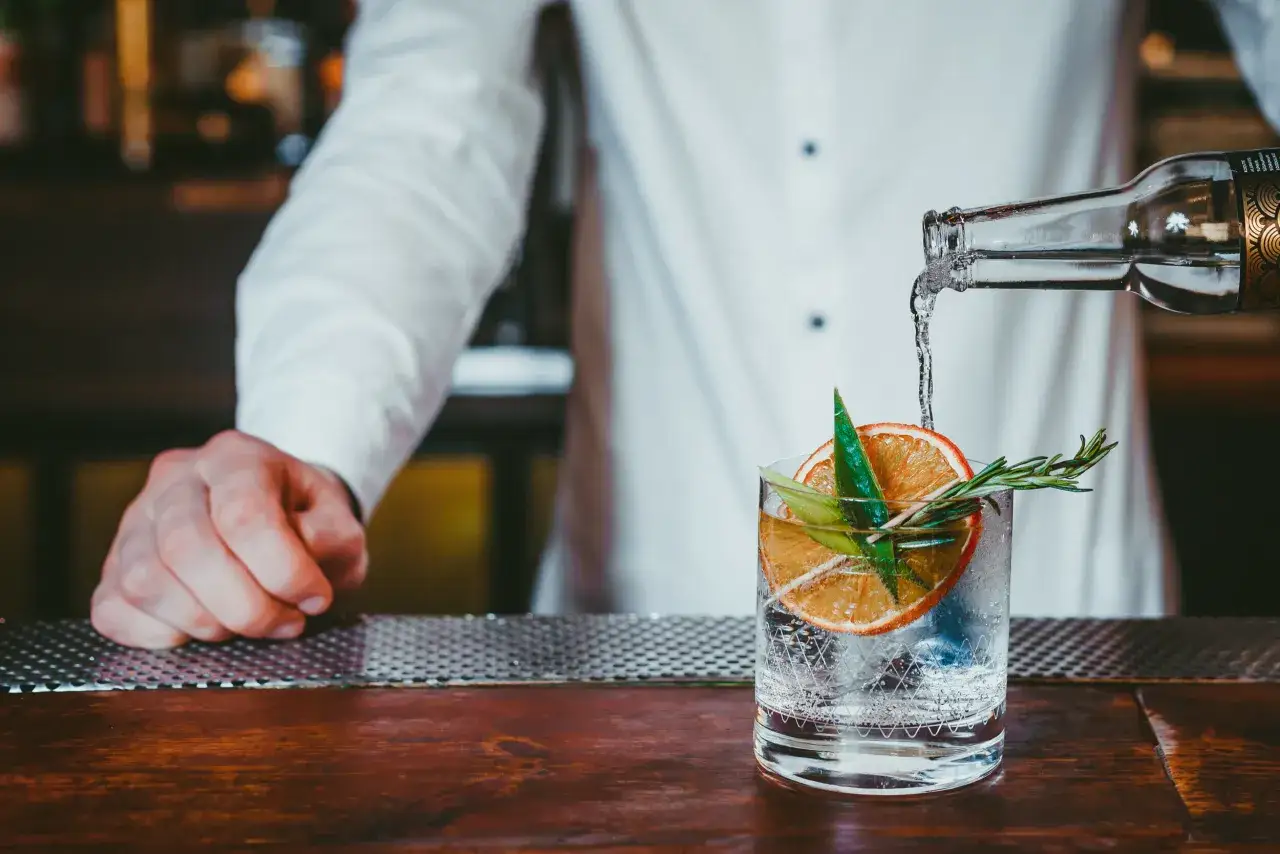 Barman nalewa wodę do szklanki z plasterkiem pomarańczy i rozmarynem. Idealny drink z ginem lubelskim lub Seagram’s do domowych drinków.