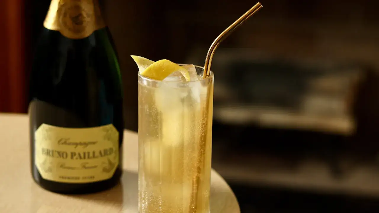 French 75 na ginie kontra French 75 na koniaku. Szklanka z drinkiem i butelka szampana.