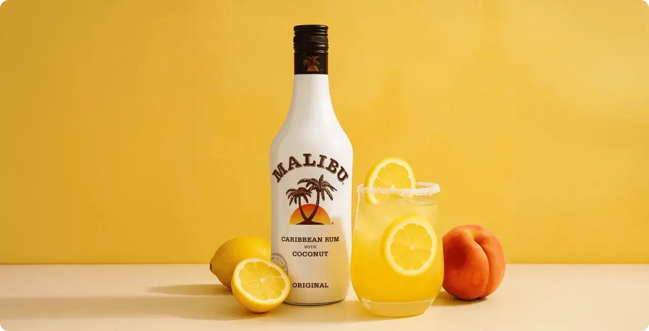 Malibu z mlekiem czy Malibu z sokiem ananasowym? Na zdjęciu butelka Malibu, drink z cytryną i brzoskwinia.