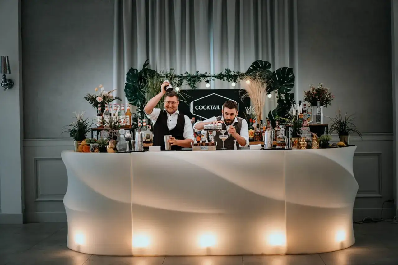Dwóch barmanów przygotowuje drinki za podświetlanym barem. Idealne rozwiązanie na wesele, sprawdź nasz drink bar na wesele cennik!