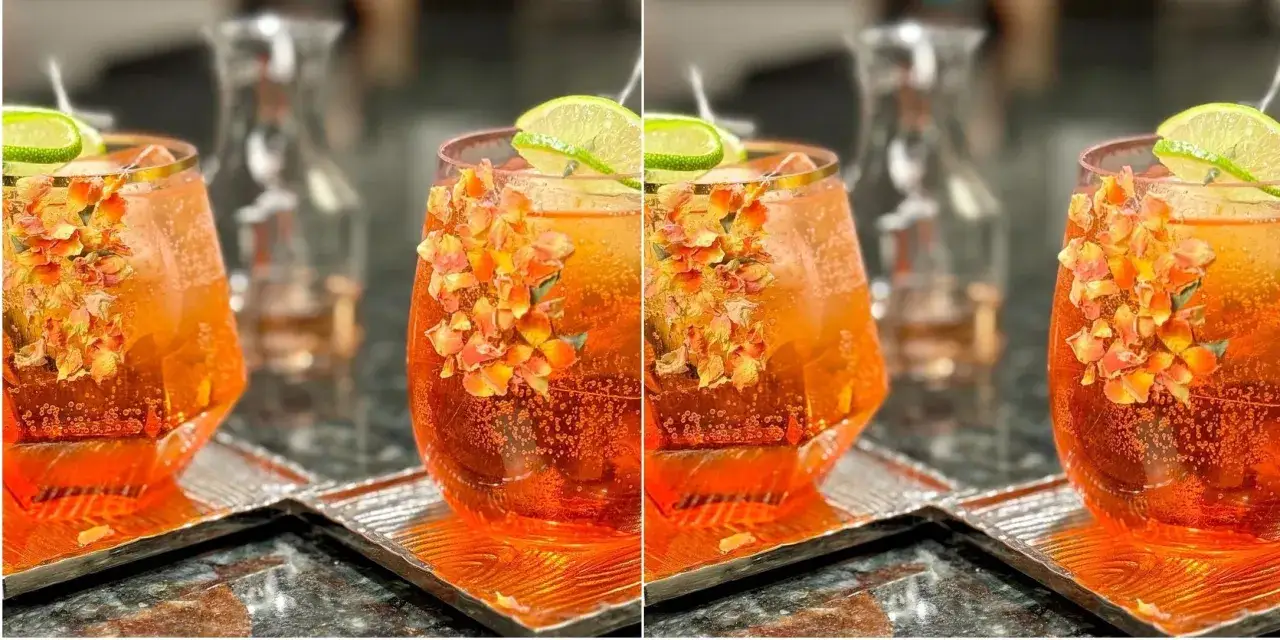 Orzeźwiający drink z aperolem, udekorowany płatkami kwiatów i plasterkiem limonki, czeka na spróbowanie.
