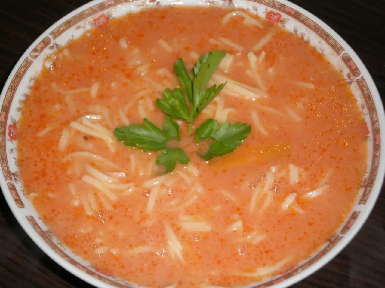 Aksamitna zupa pomidorowa z makaronem, ozdobiona natką pietruszki. Idealna na obiad, a jej przepis jest prosty i szybki.