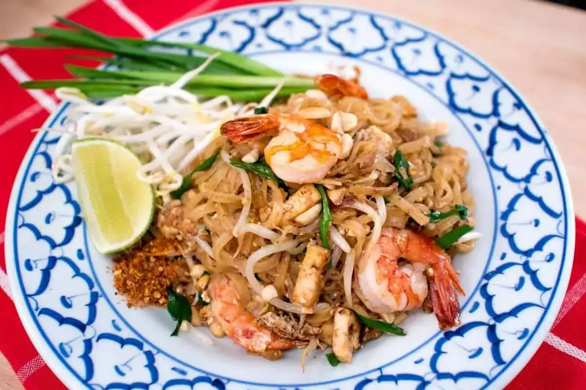 Pyszny Pad Thai przepis na talerzu: makaron ryżowy z krewetkami, kiełkami fasoli mung, szczypiorkiem i ćwiartką limonki.